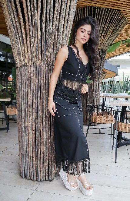 Una mujer con un vestido negro está parada junto a un árbol.