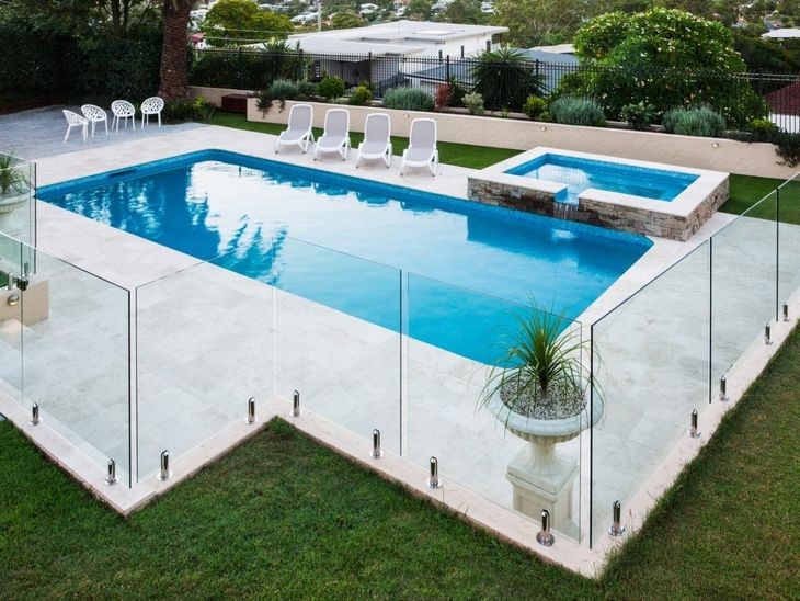 Swimming pool with glass fencing, sun loungers, and a small hot tub surrounded by landscaping.