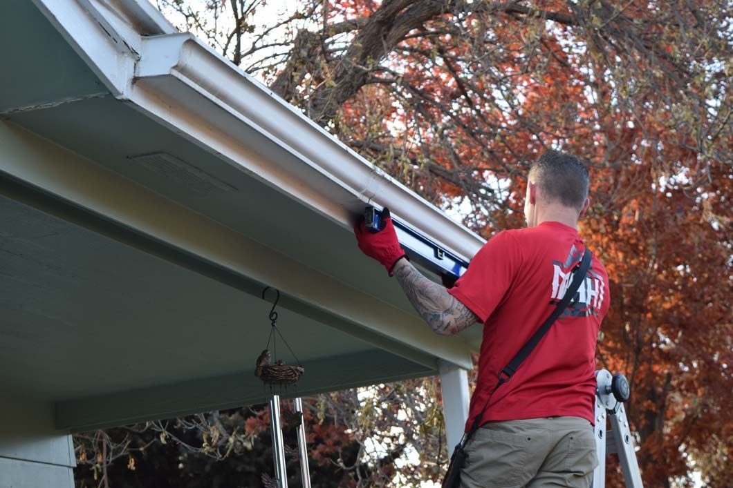 A man is standing on a ladder fixing a gutter on a house.