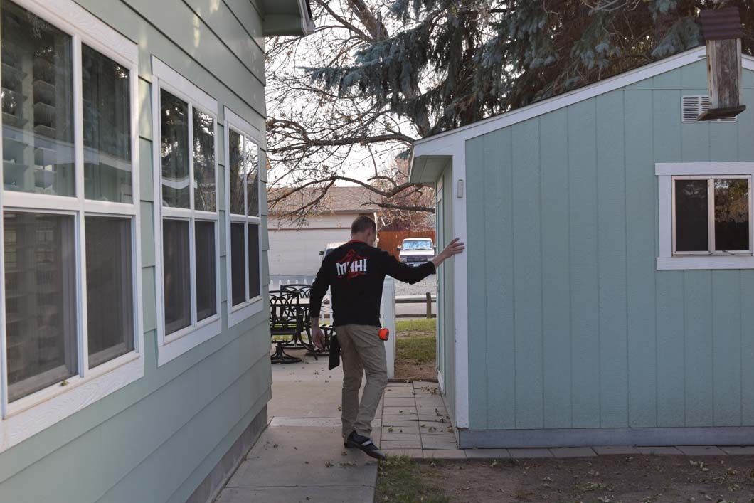 A man in a black shirt is standing in front of a house.