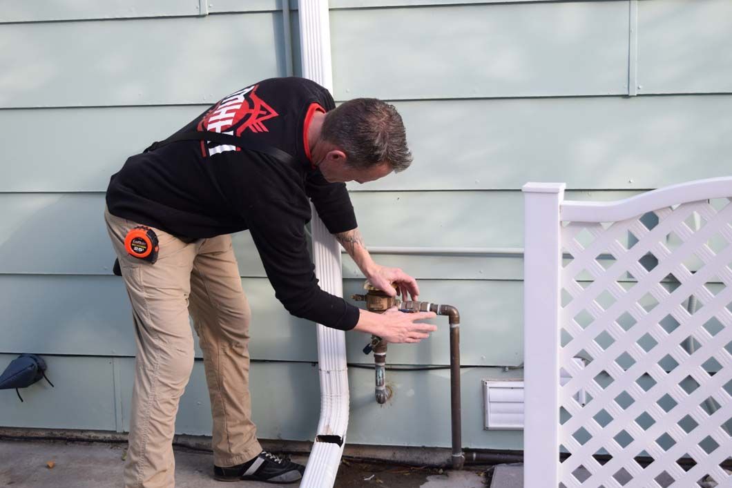 A man is working on a pipe outside of a house.