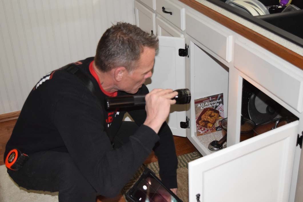 A man is looking under a kitchen sink with a magnifying glass