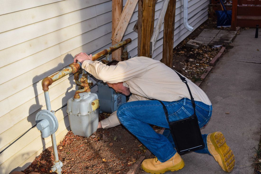 A man is kneeling down to fix a gas meter on the side of a house.
