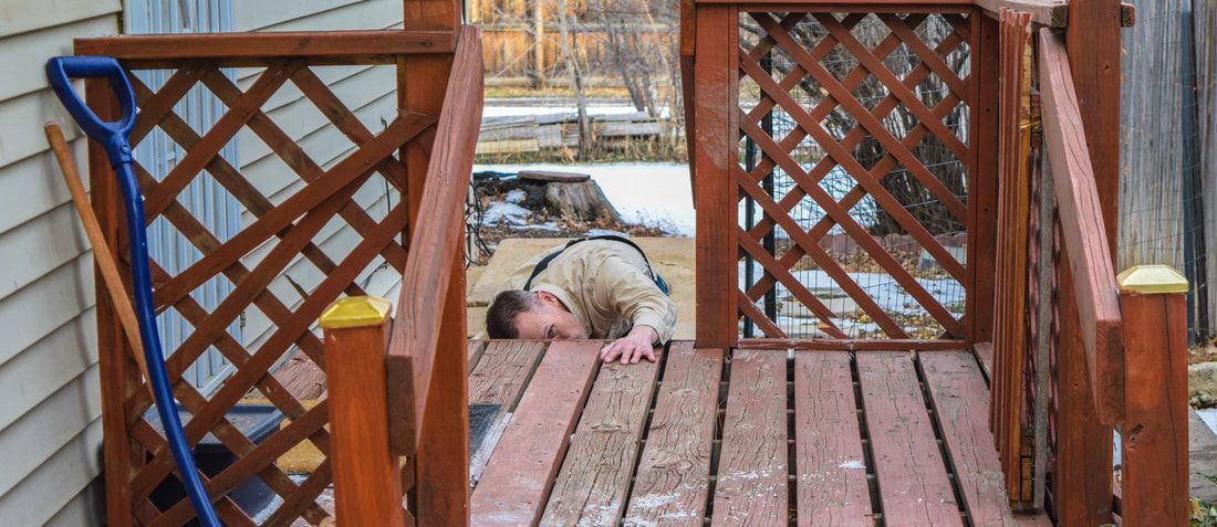 A man is laying on a wooden deck next to a house.