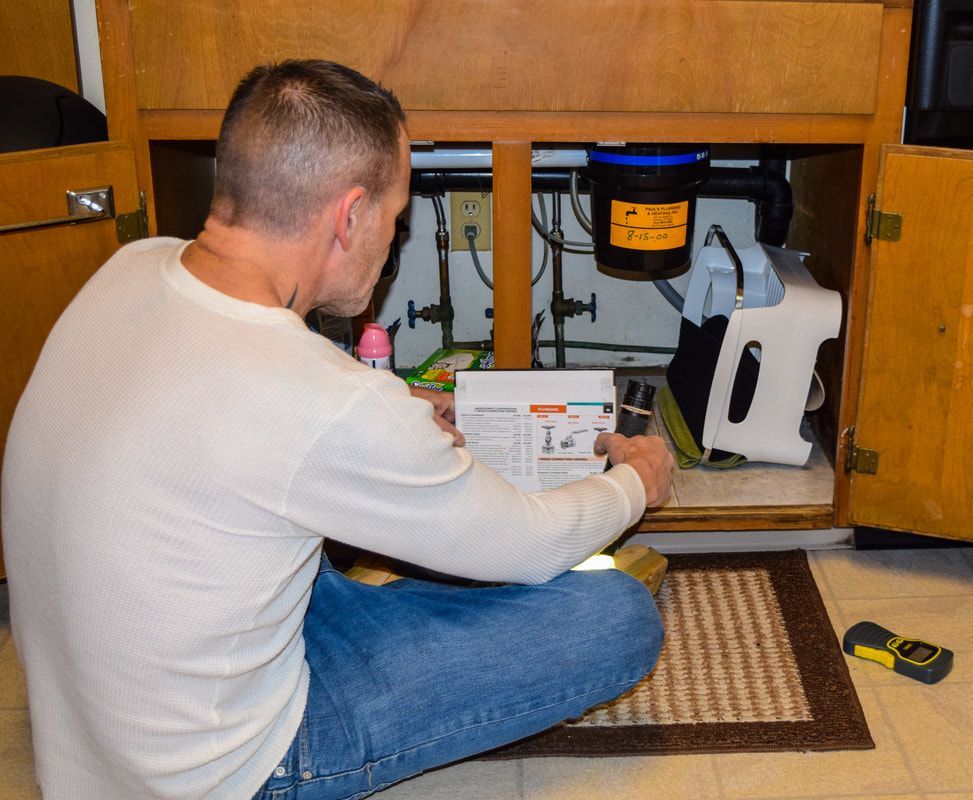A man is kneeling down under a sink looking at a paper