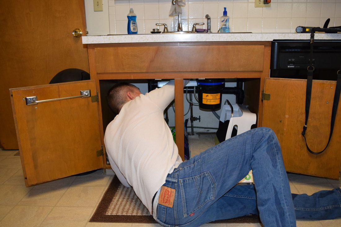 A man is kneeling under a sink in a kitchen