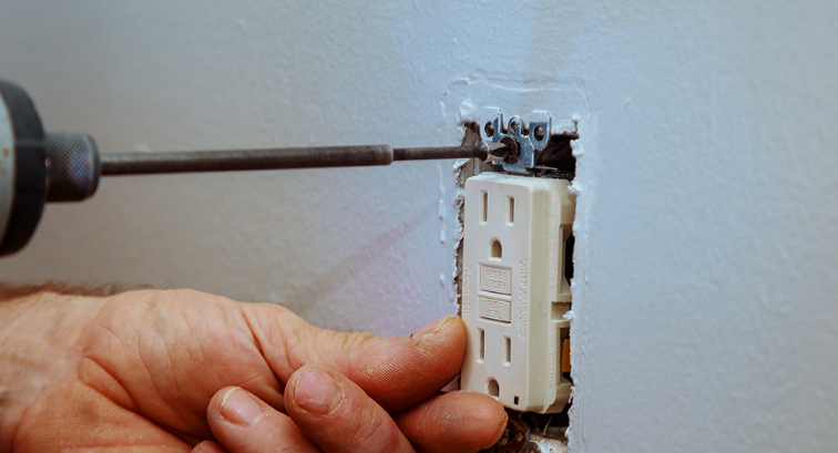 A person is using a screwdriver to fix an electrical outlet on a wall.