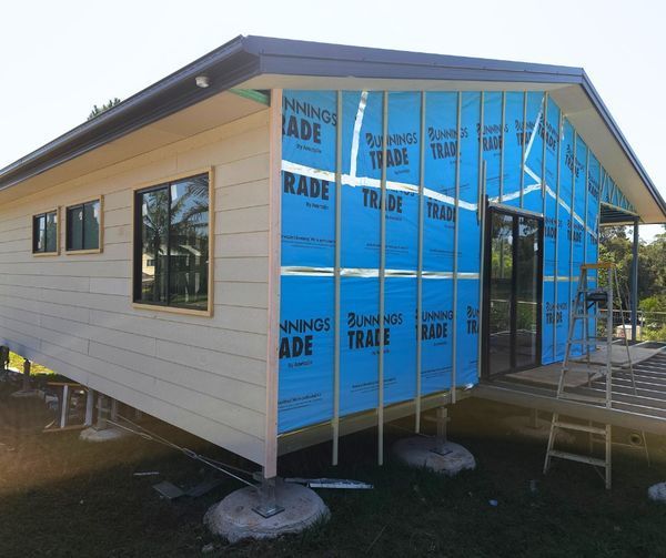 House under construction, with blue building wrap visible on the exterior wall.