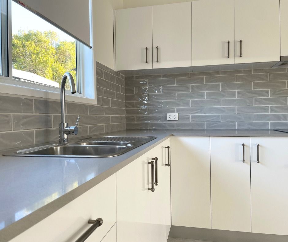 Bright, modern kitchen with white cabinets, gray countertops and backsplash, stainless steel sink.