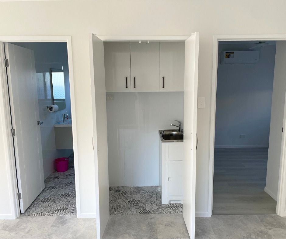Interior view with a laundry area centered between two doorways. The laundry area includes a sink, cabinets, and a cabinet below the sink.