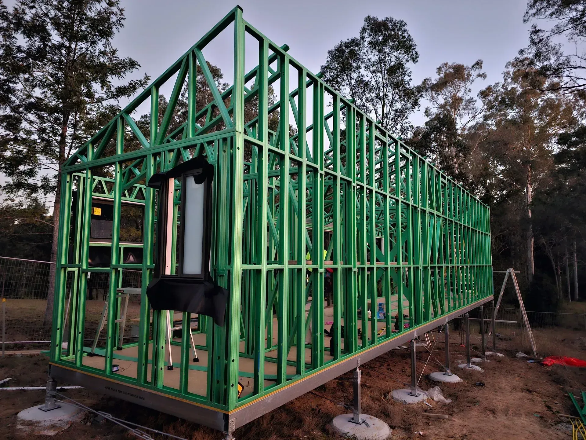 Green wooden frame of a house under construction on concrete footings outdoors.