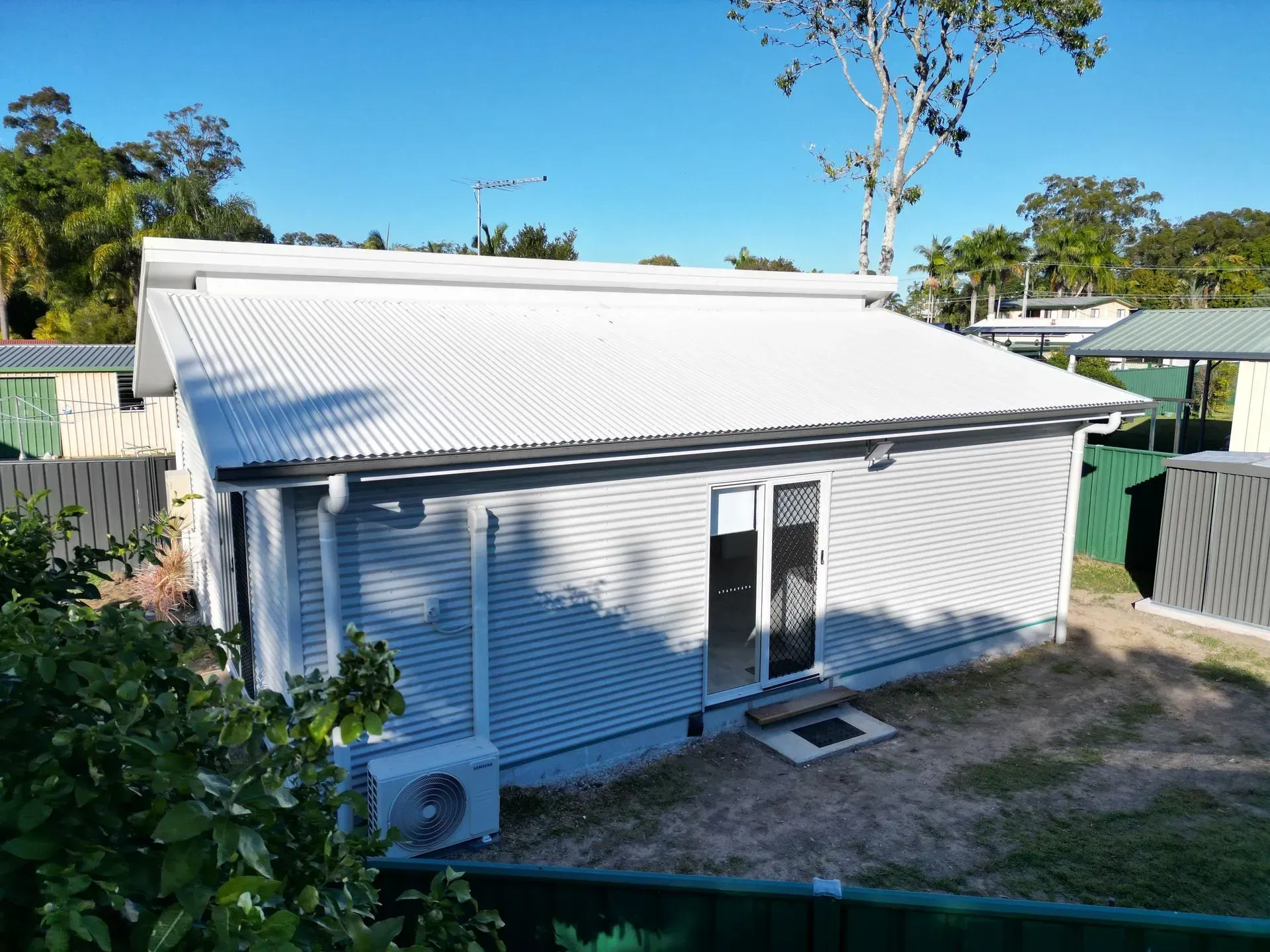 A light gray, corrugated metal building with a white roof and an air conditioning unit outside.
