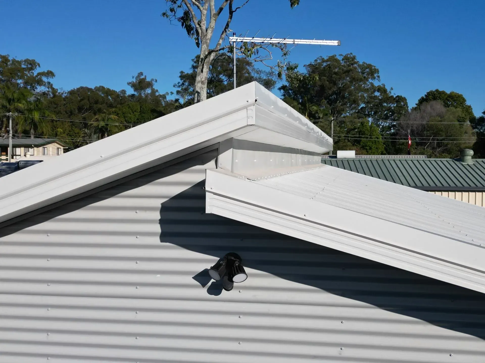 A light gray corrugated metal roof with white trim and an antenna against a blue sky.