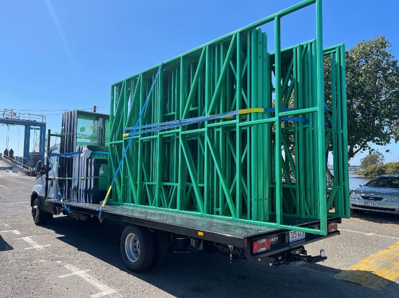 Green metal frame construction panels secured on a flatbed truck outdoors, near water.