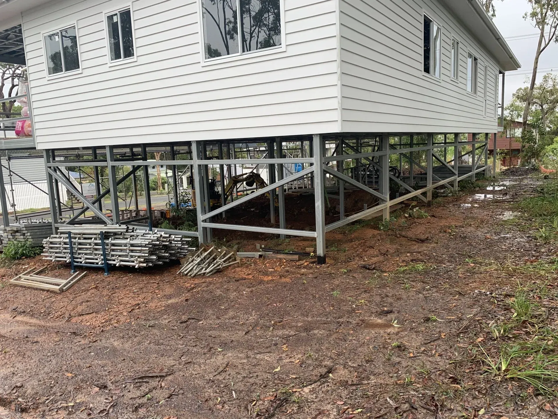 White house on stilts under construction, on a dirt lot.