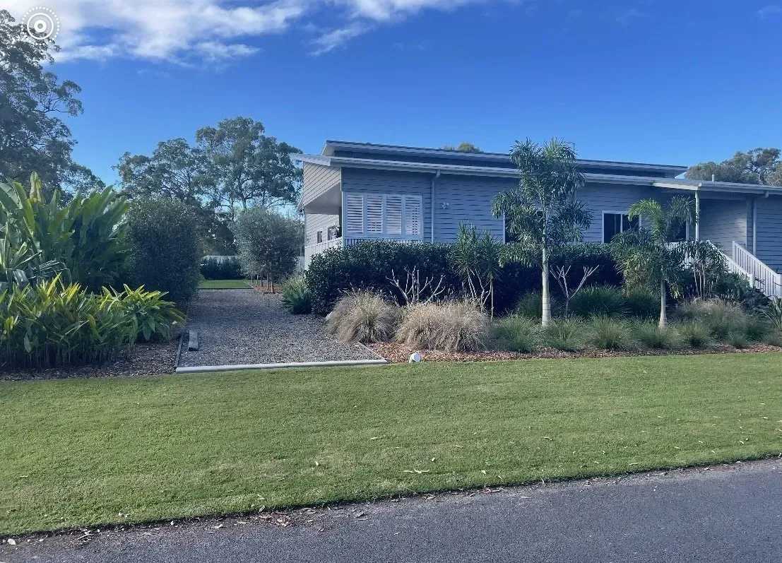 A modern house with gray siding sits behind a manicured lawn and landscaping on a sunny day.