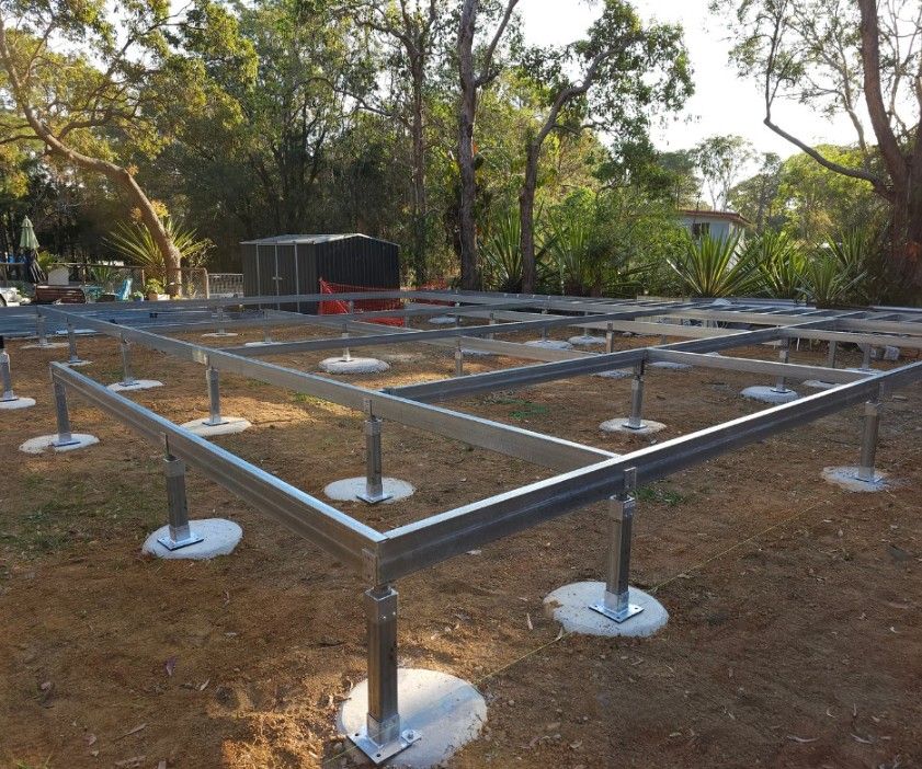 Metal framework foundation on concrete pads, outdoors in a yard, under trees, preparing for a structure.