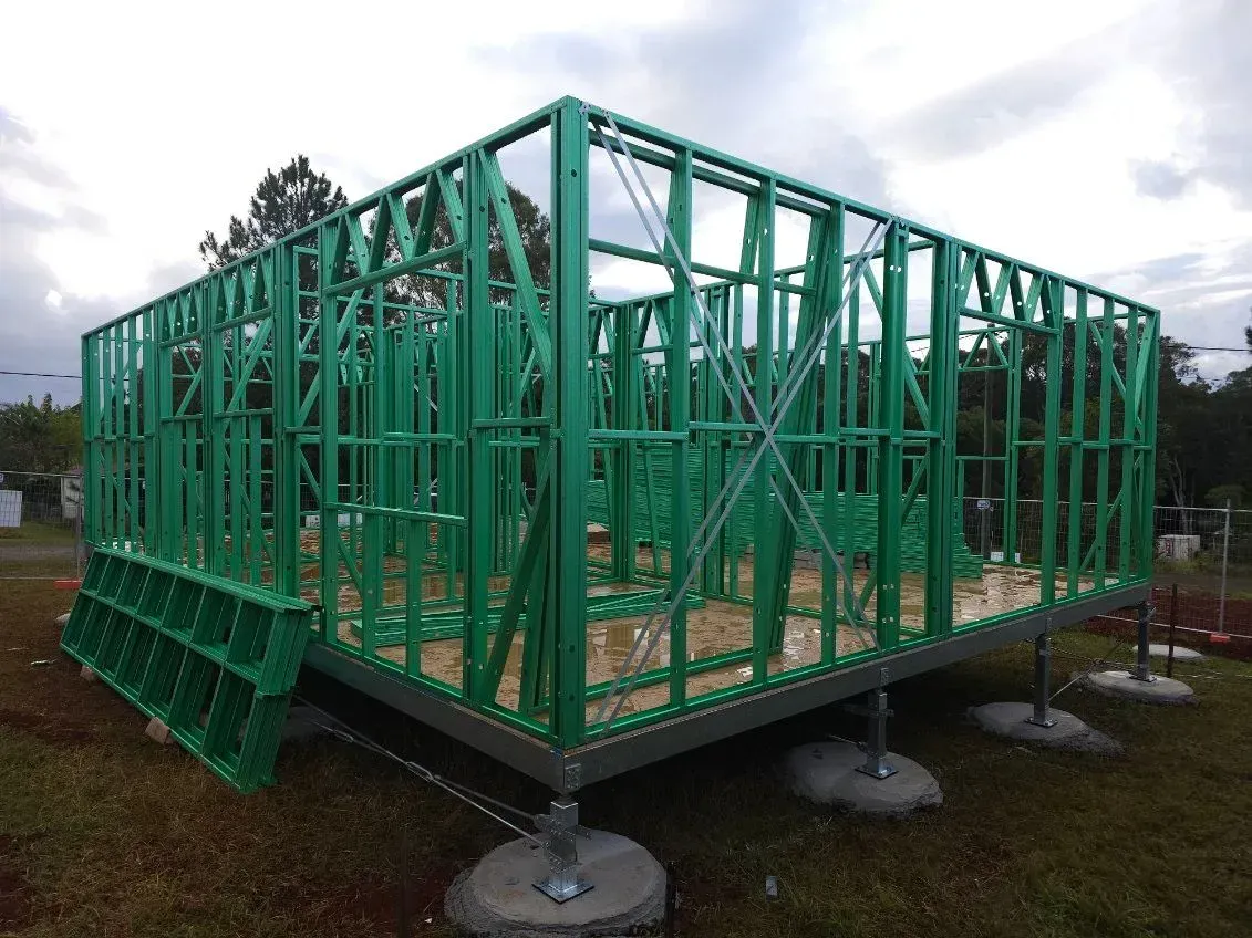 Green framed building under construction on concrete blocks.