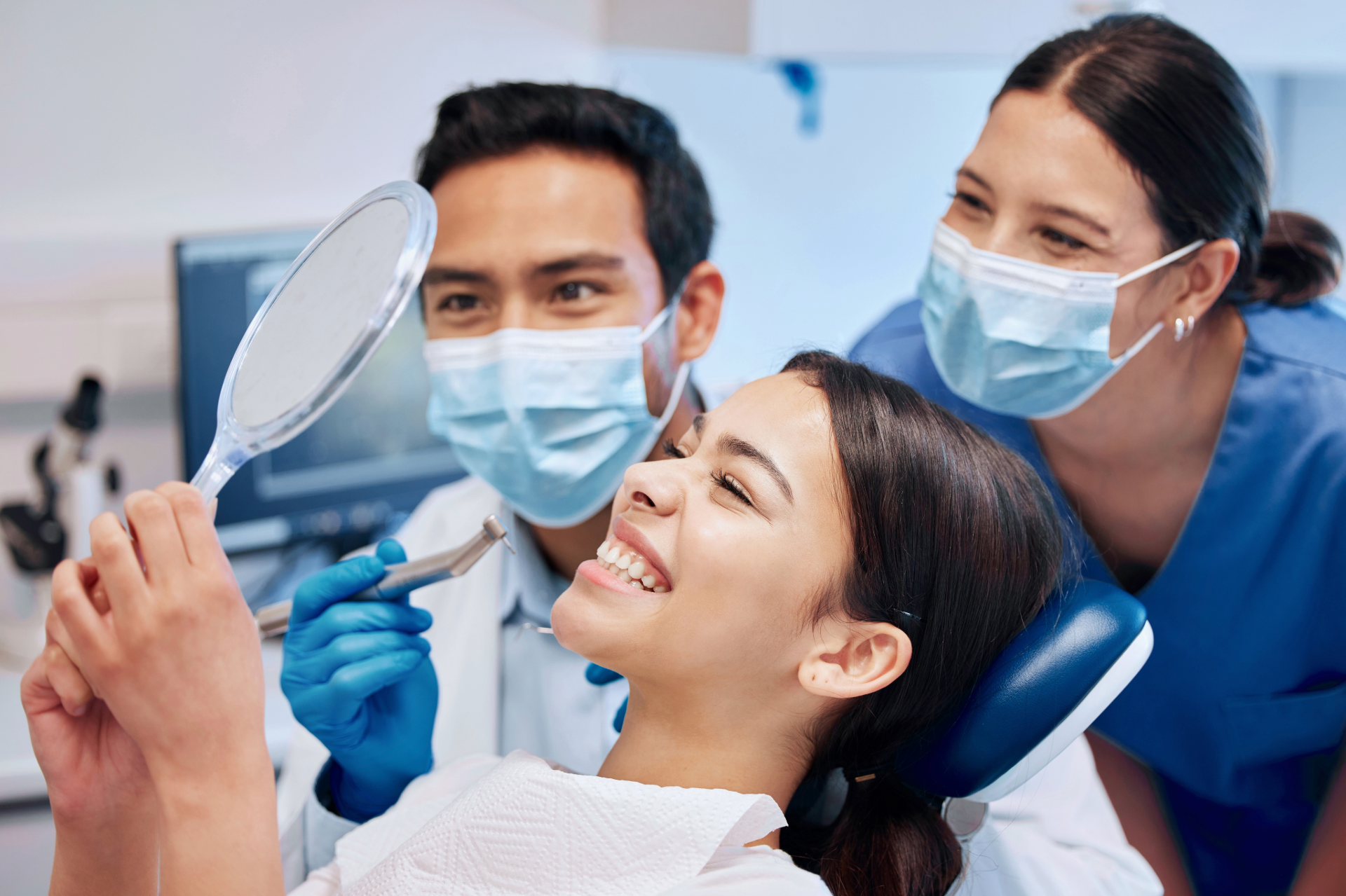 Dentist and assistant examining a patient's teeth with a mirror, inside a dental office.