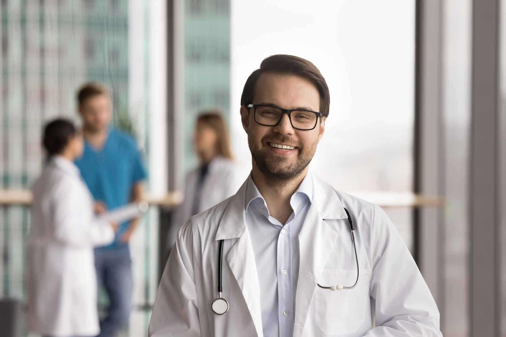Smiling doctor in a white coat with colleagues in the background.