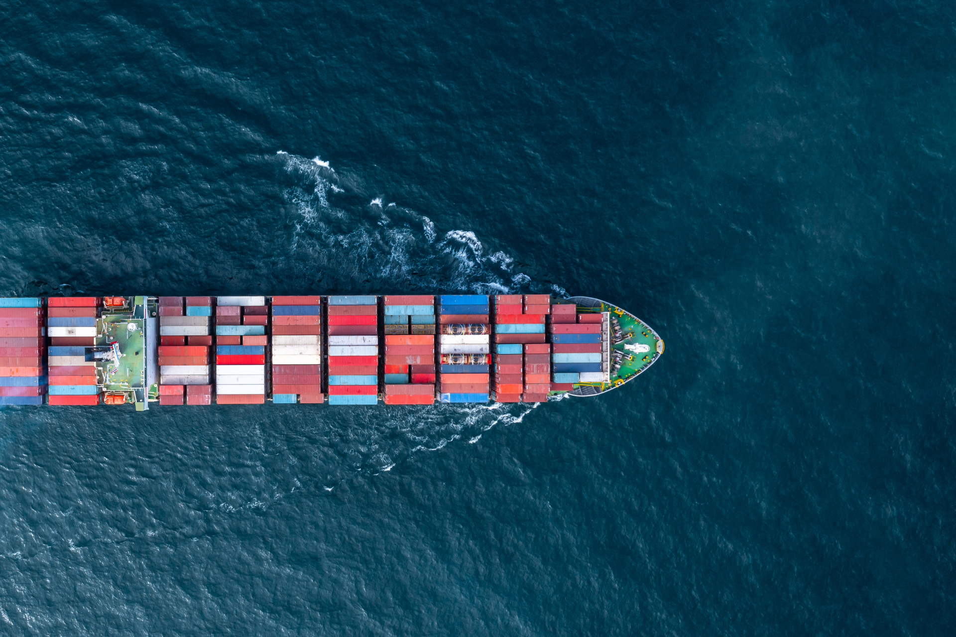 Cargo ship sailing across deep blue ocean, carrying colorful shipping containers.