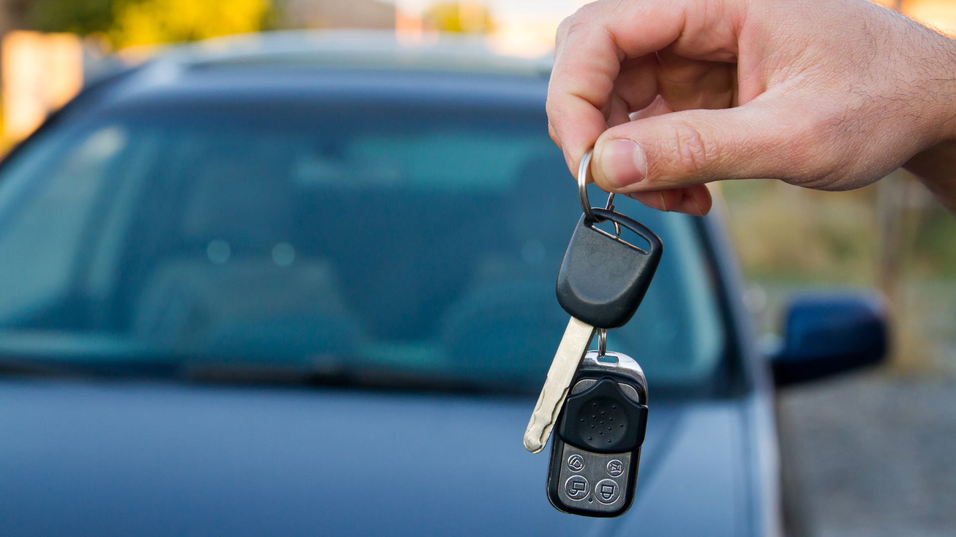 A person is holding a pair of car keys in front of a car.