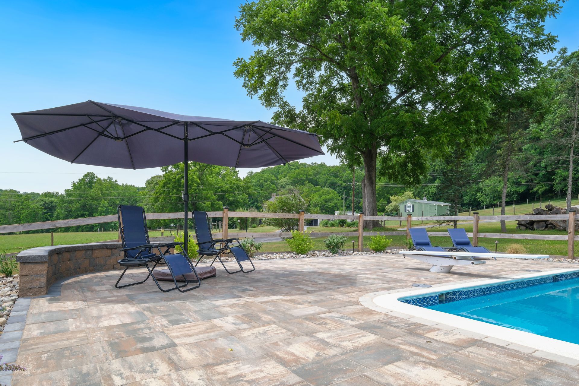 A large umbrella is sitting on a patio next to a swimming pool.