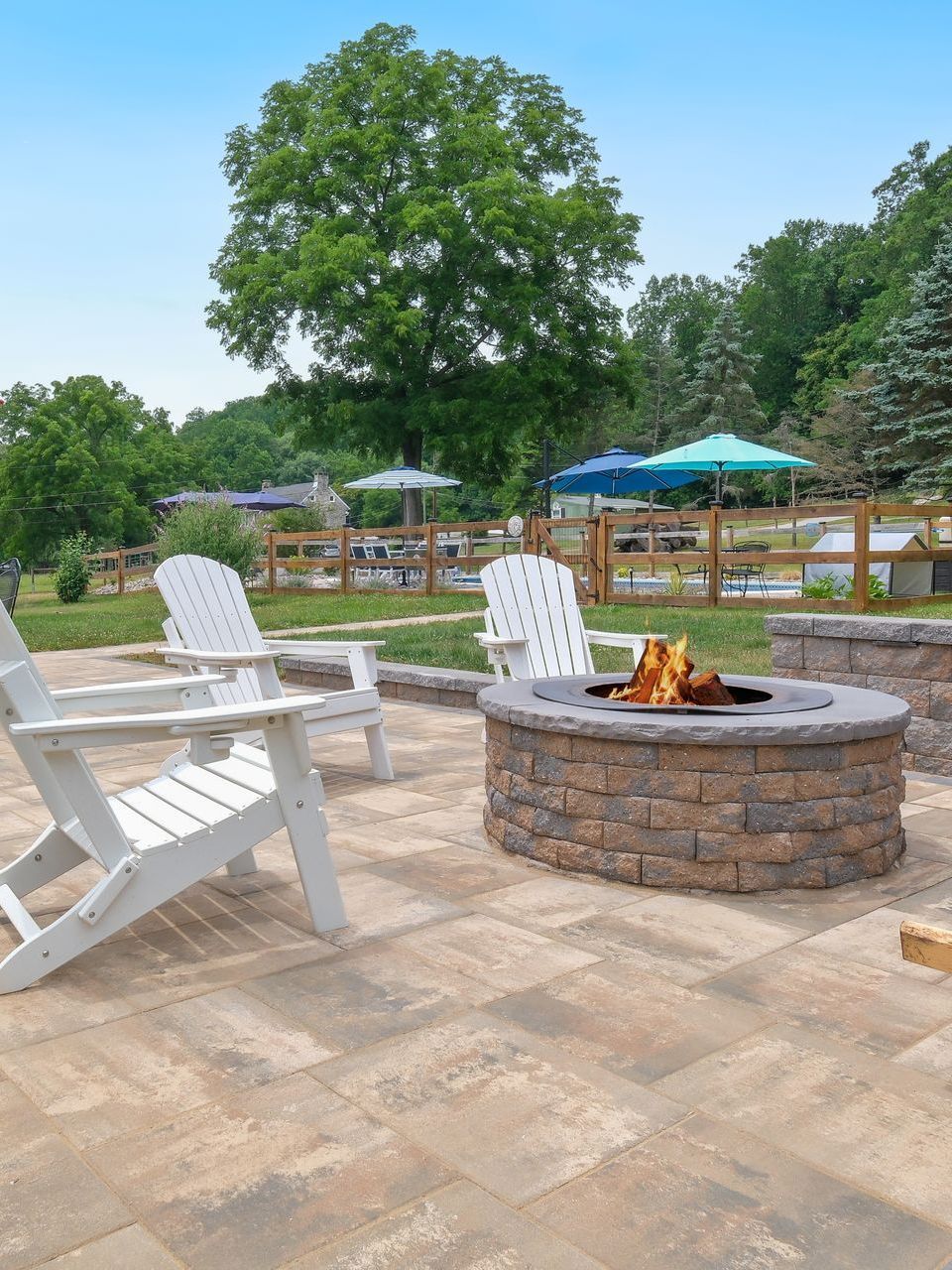 A fire pit on a patio with chairs and umbrellas.