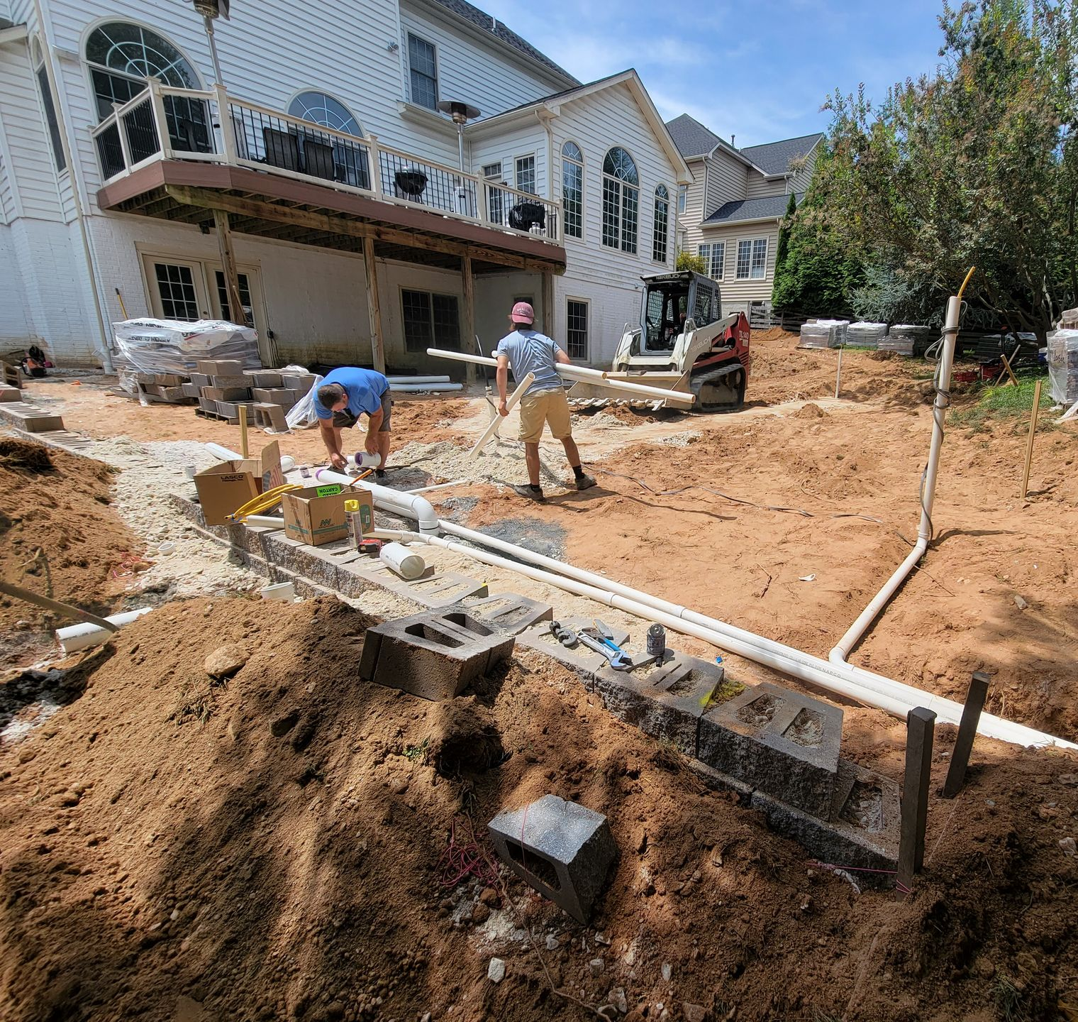 Construction workers building a backyard patio near a multi-story home.
