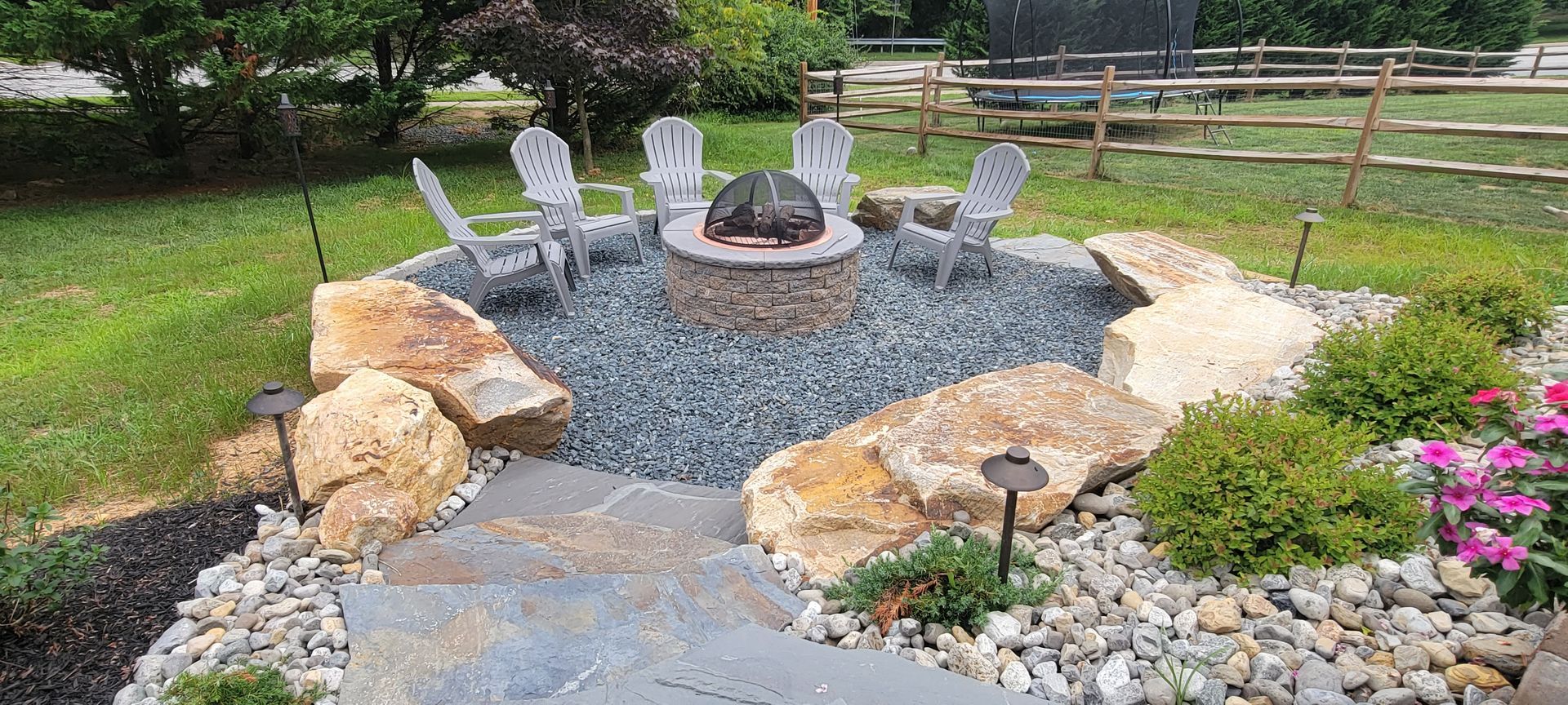 A fire pit surrounded by rocks and chairs in a backyard.