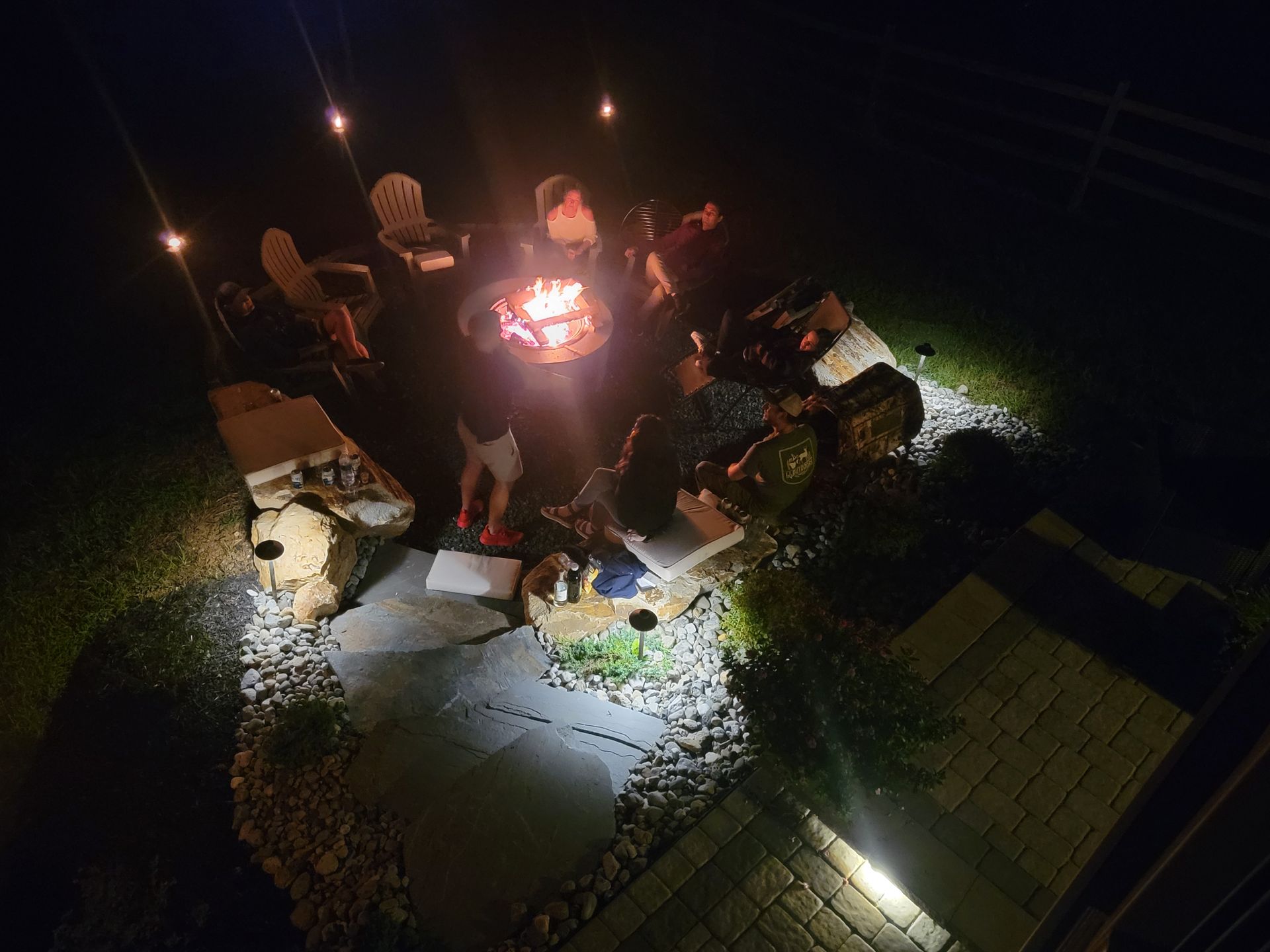 A group of people are sitting around a fire pit at night.