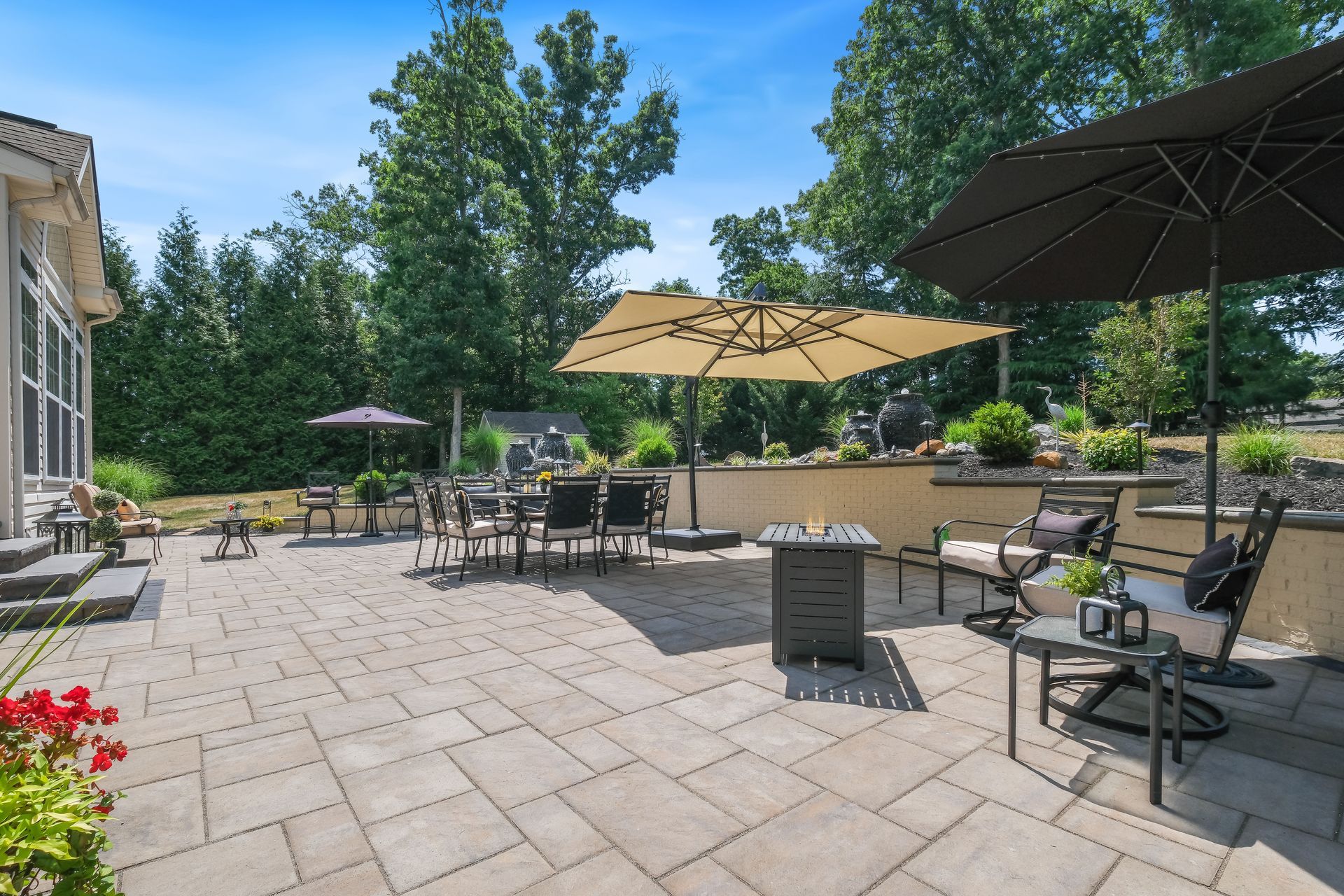 A large patio with umbrellas , chairs , tables and a fire pit.