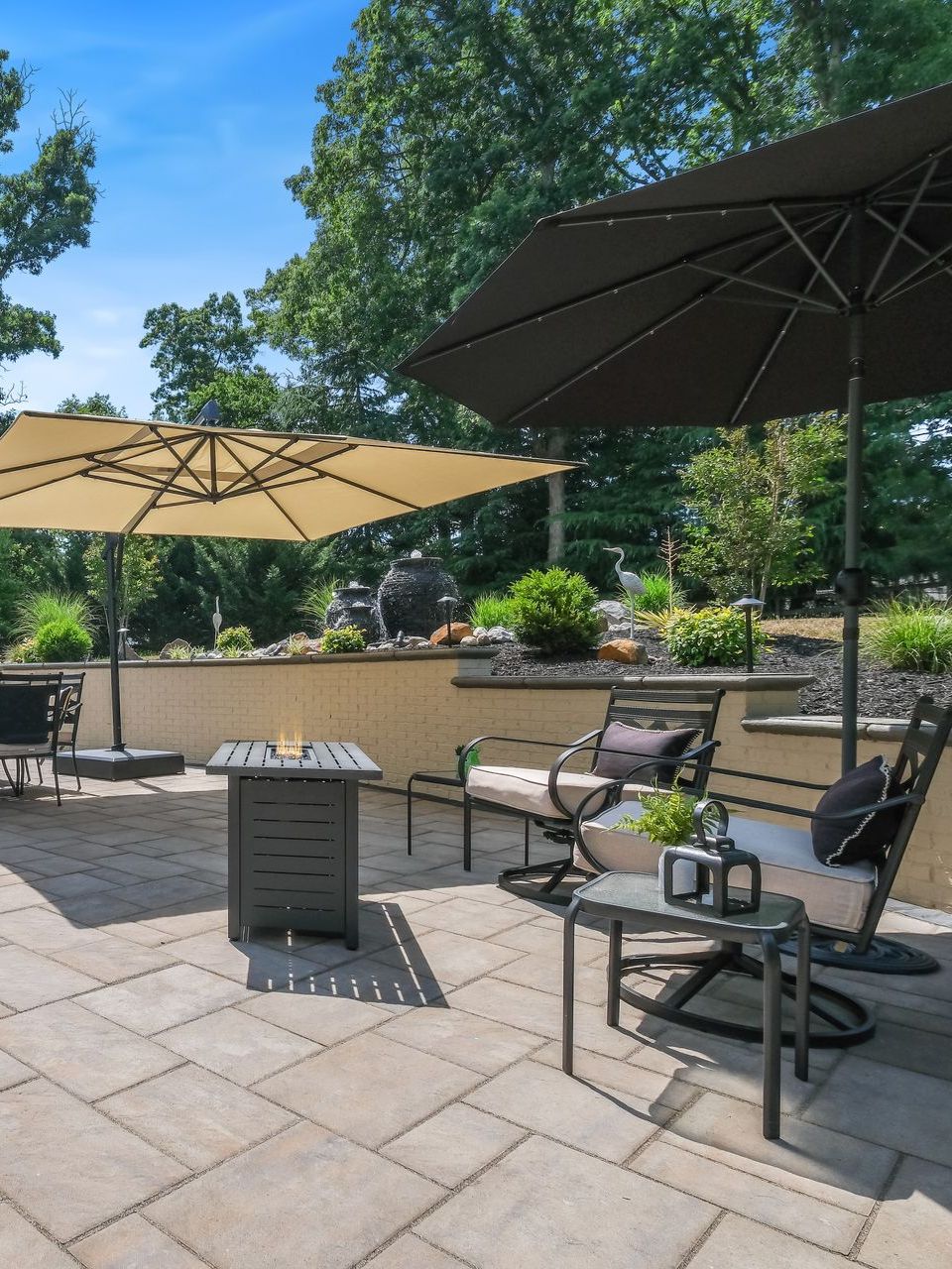 A patio with umbrellas , chairs , tables and a fire pit.