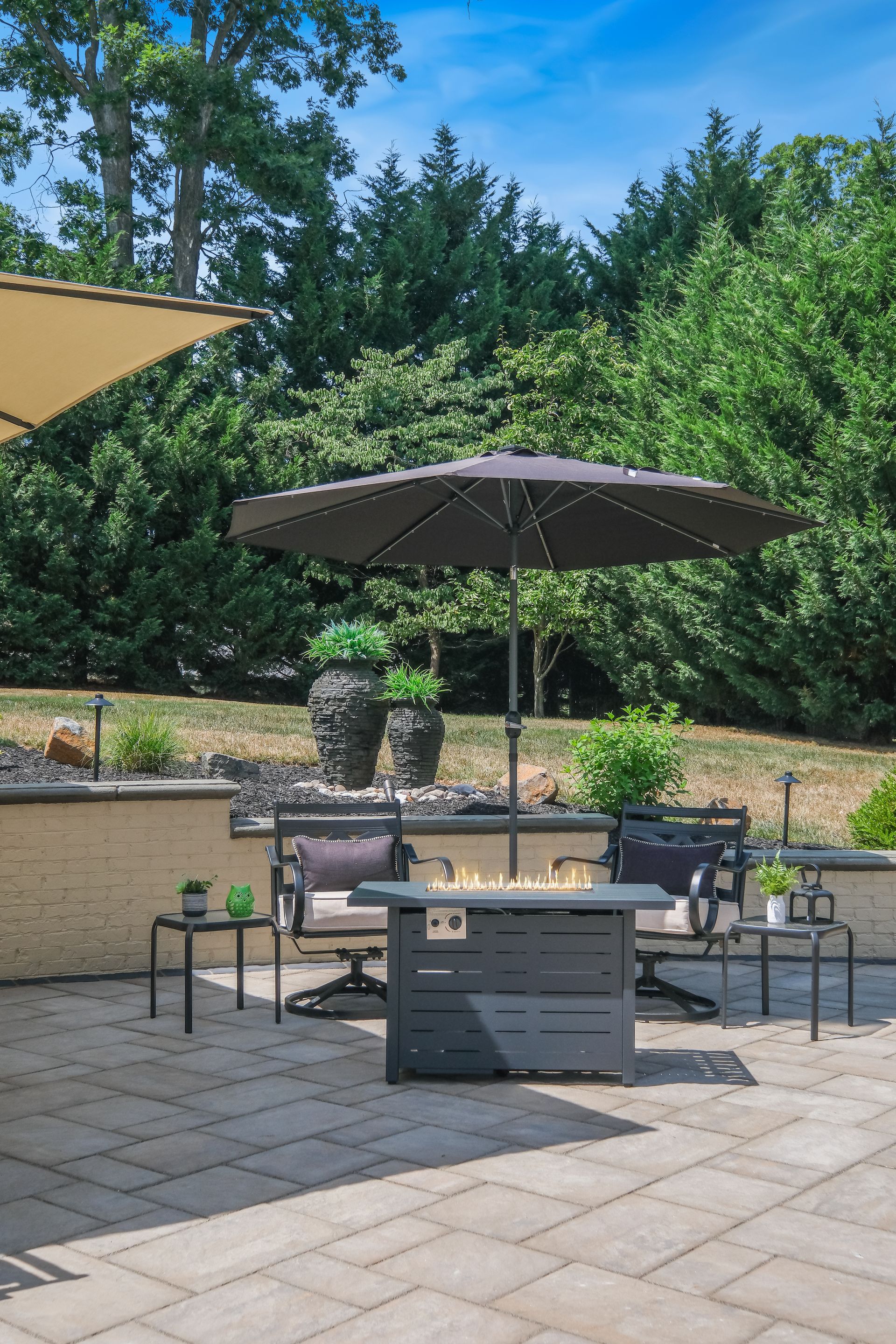 A patio with a fire pit , chairs , tables and umbrellas.