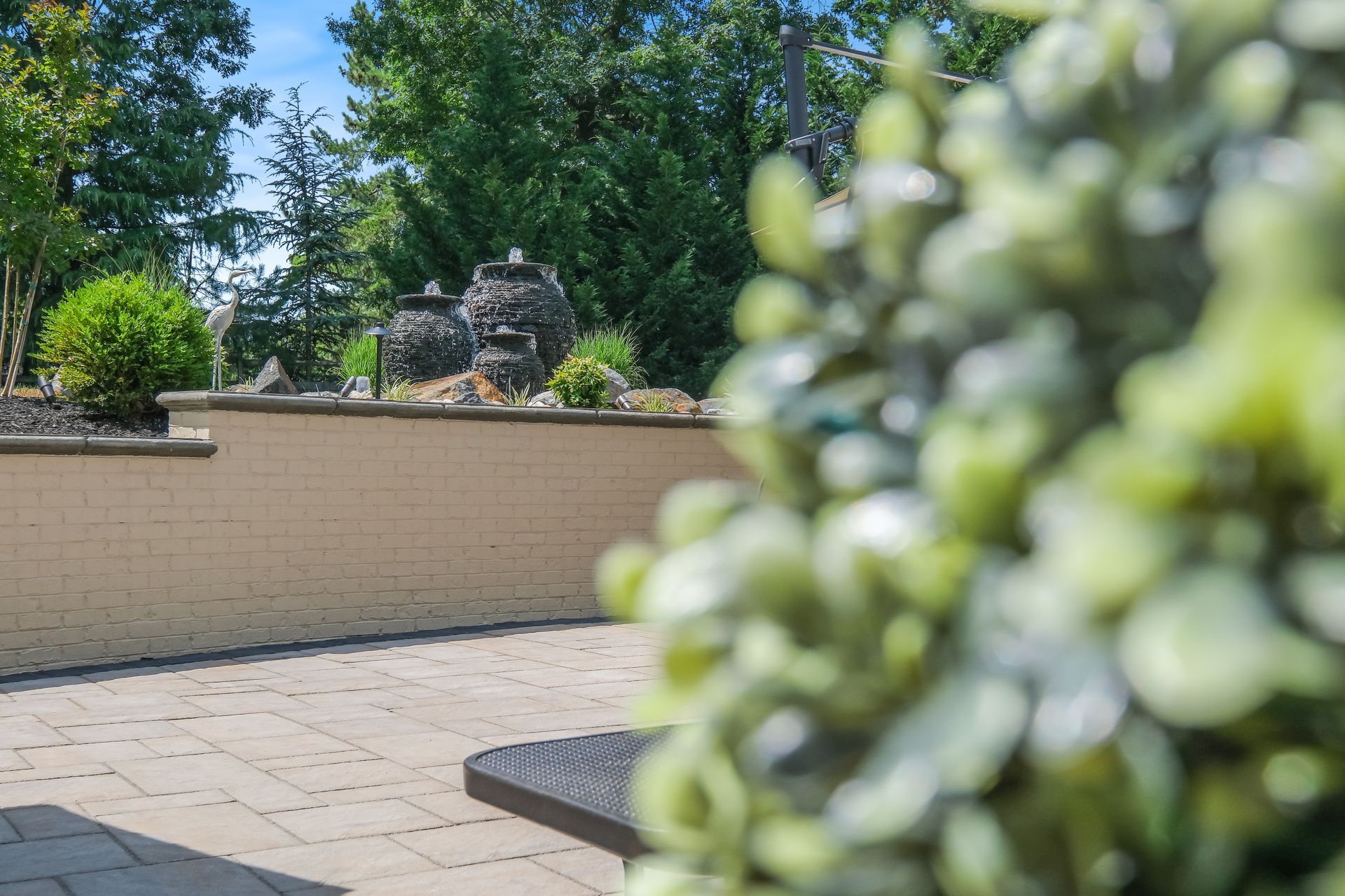 A patio with a brick wall and a bush in the foreground.