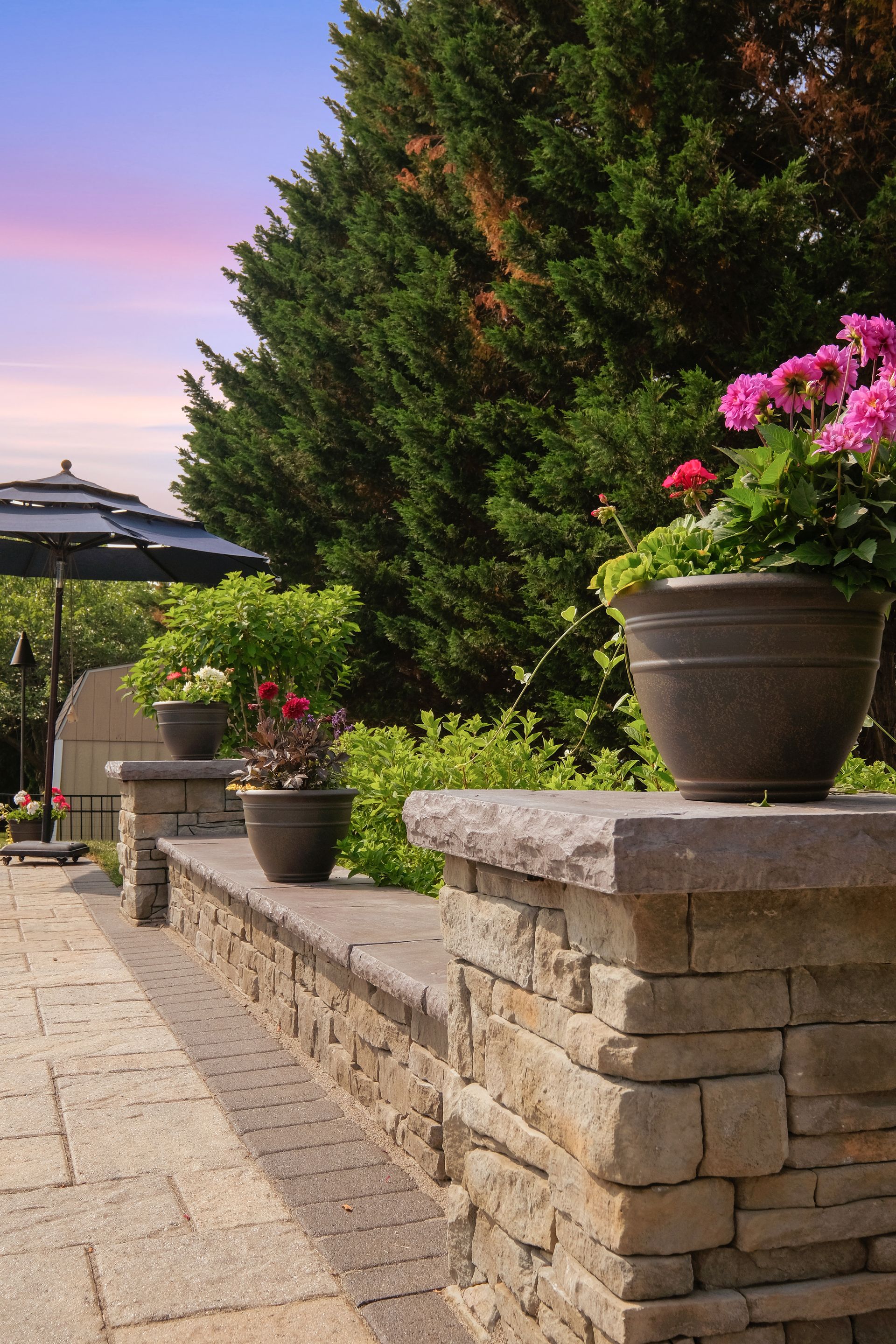 A stone wall with potted plants on it and trees in the background.