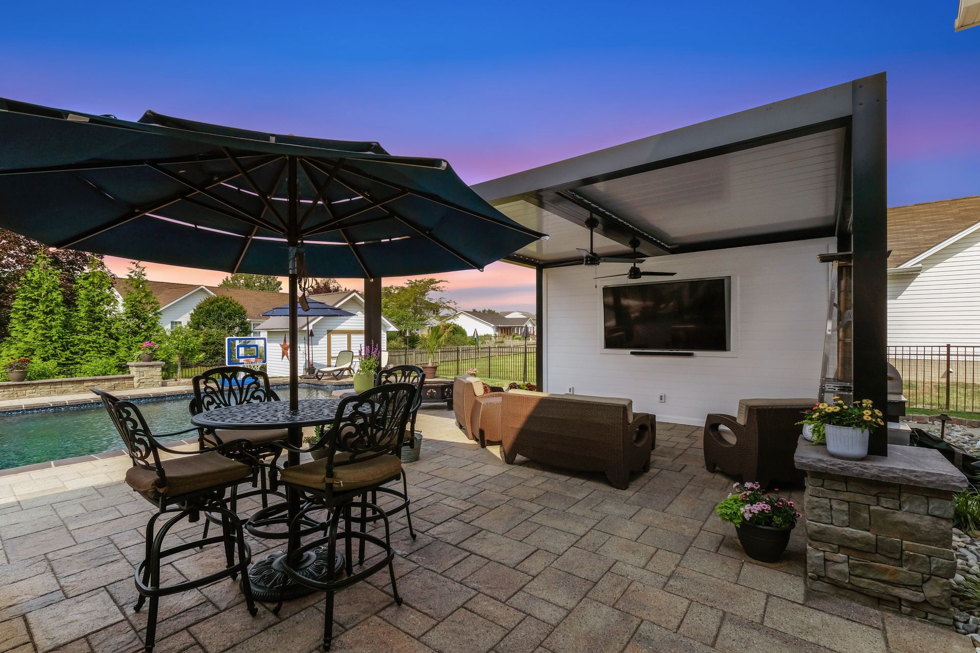 A patio with a table and chairs under an umbrella next to a pool.