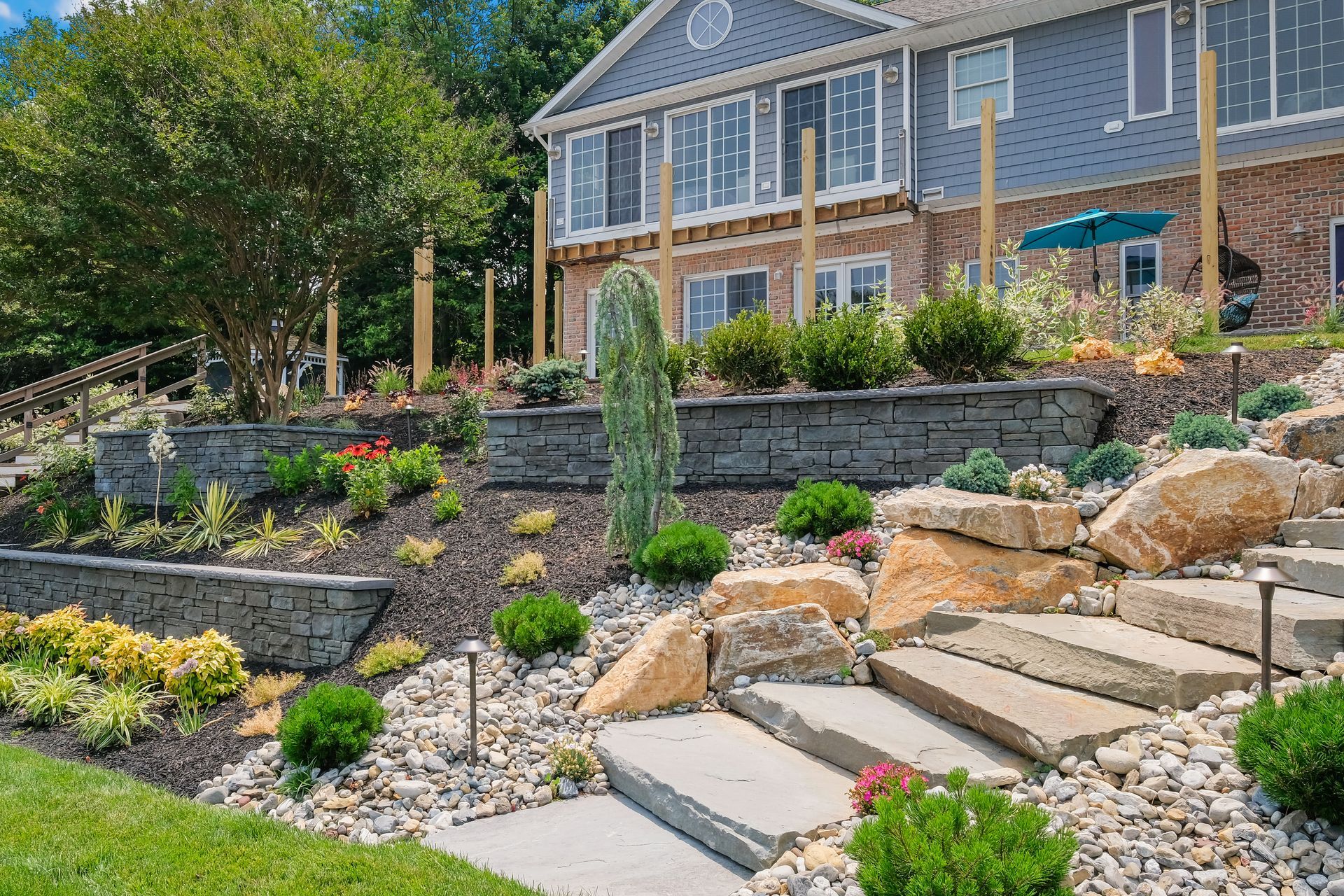 A large house with stairs leading up to it is surrounded by rocks and plants.