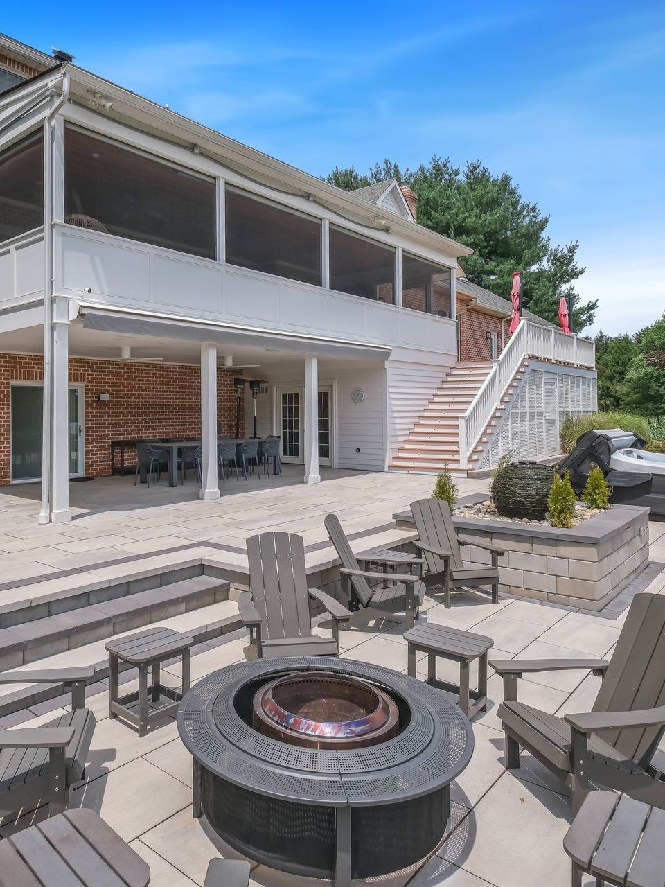 A patio with a fire pit and chairs in front of a large house.