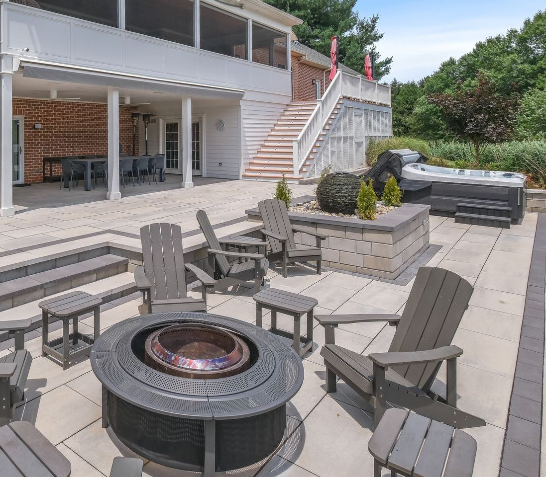 Patio with fire pit, seating, hot tub, and two-story house.