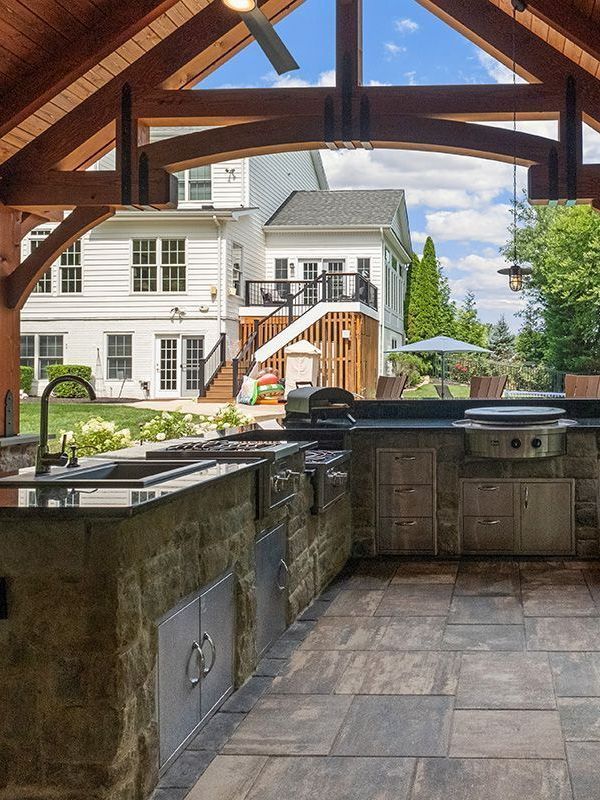 A kitchen with a sink , stove , and grill with a view of a house in the background.