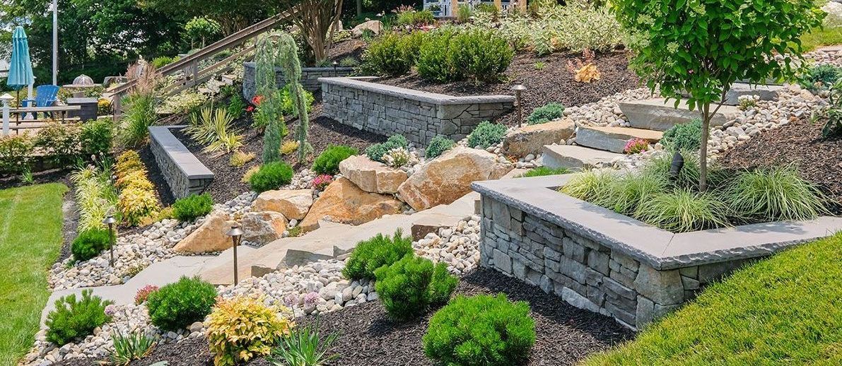 A lush green garden with a stone wall and steps leading up to a house.
