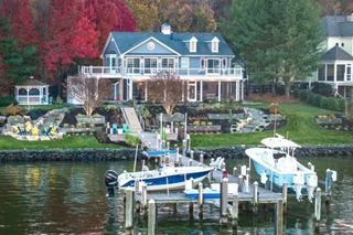 A large house sits on the shore of a lake with boats docked in front of it.