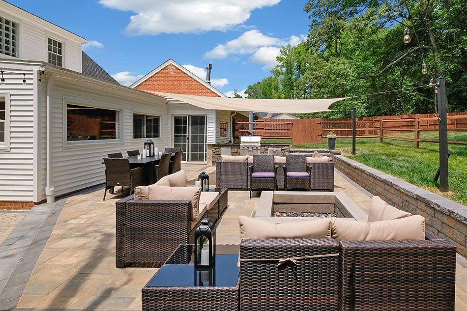 A patio with wicker furniture and a fire pit in front of a house.