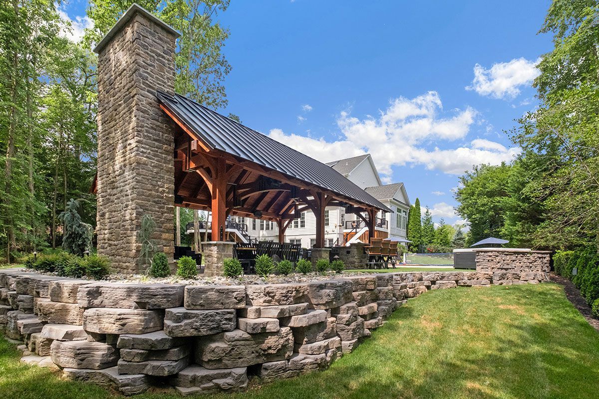 A stone pavilion with a fireplace and a stone wall in the backyard of a house.