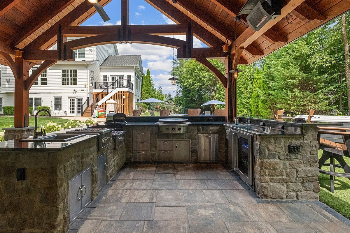 A large outdoor kitchen with a wooden roof and stainless steel appliances.