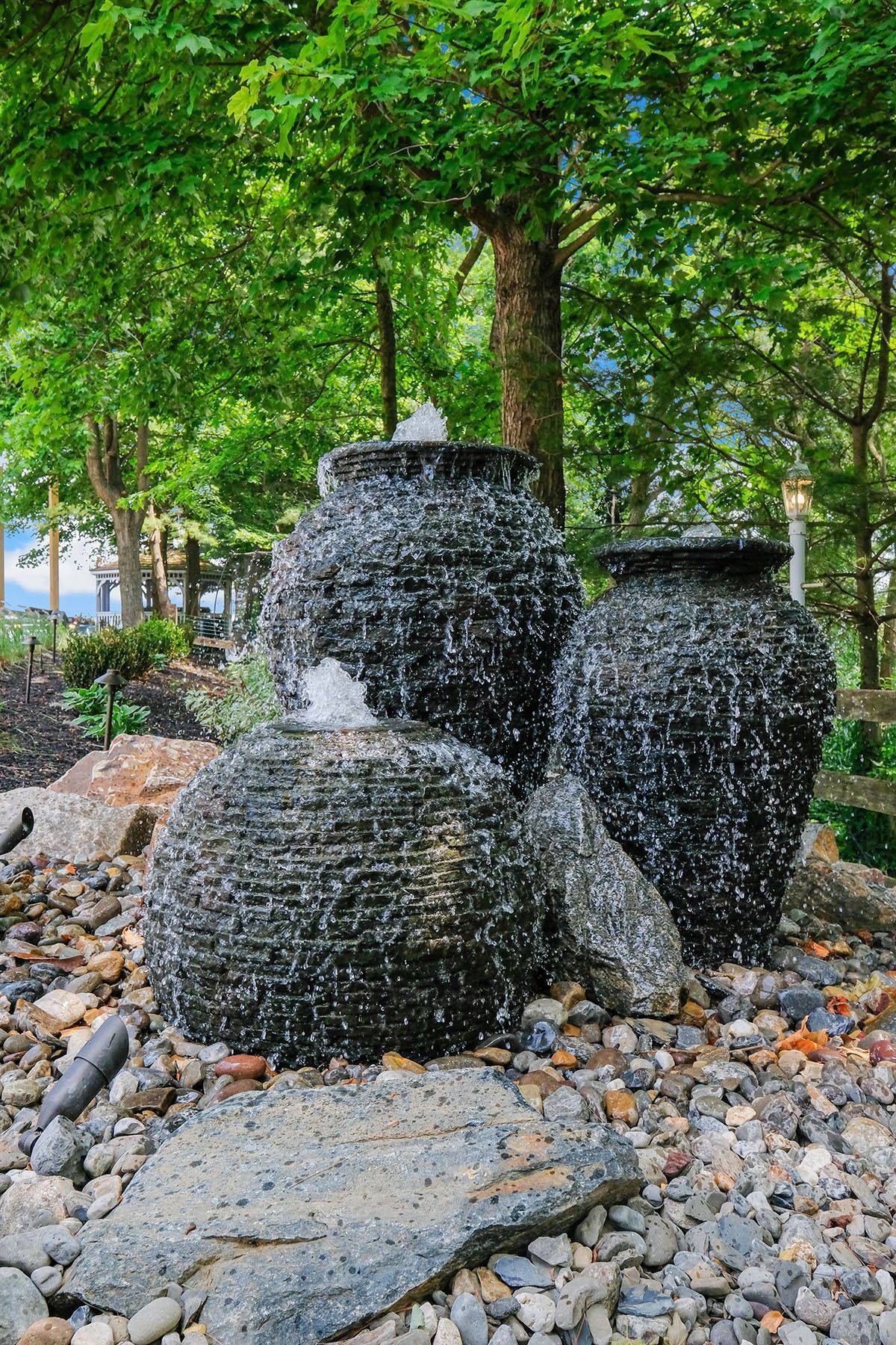 There is a fountain in the middle of a rocky area surrounded by trees.