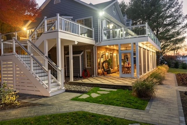 A large house with a large deck and stairs is lit up at night.