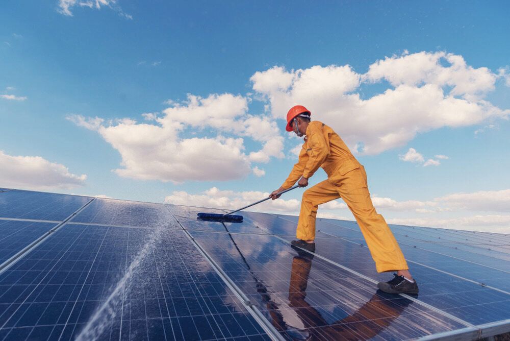 A Man Is Cleaning Solar Panels With A Broom — Central West Budget Tree Services in Dubbo, NSW