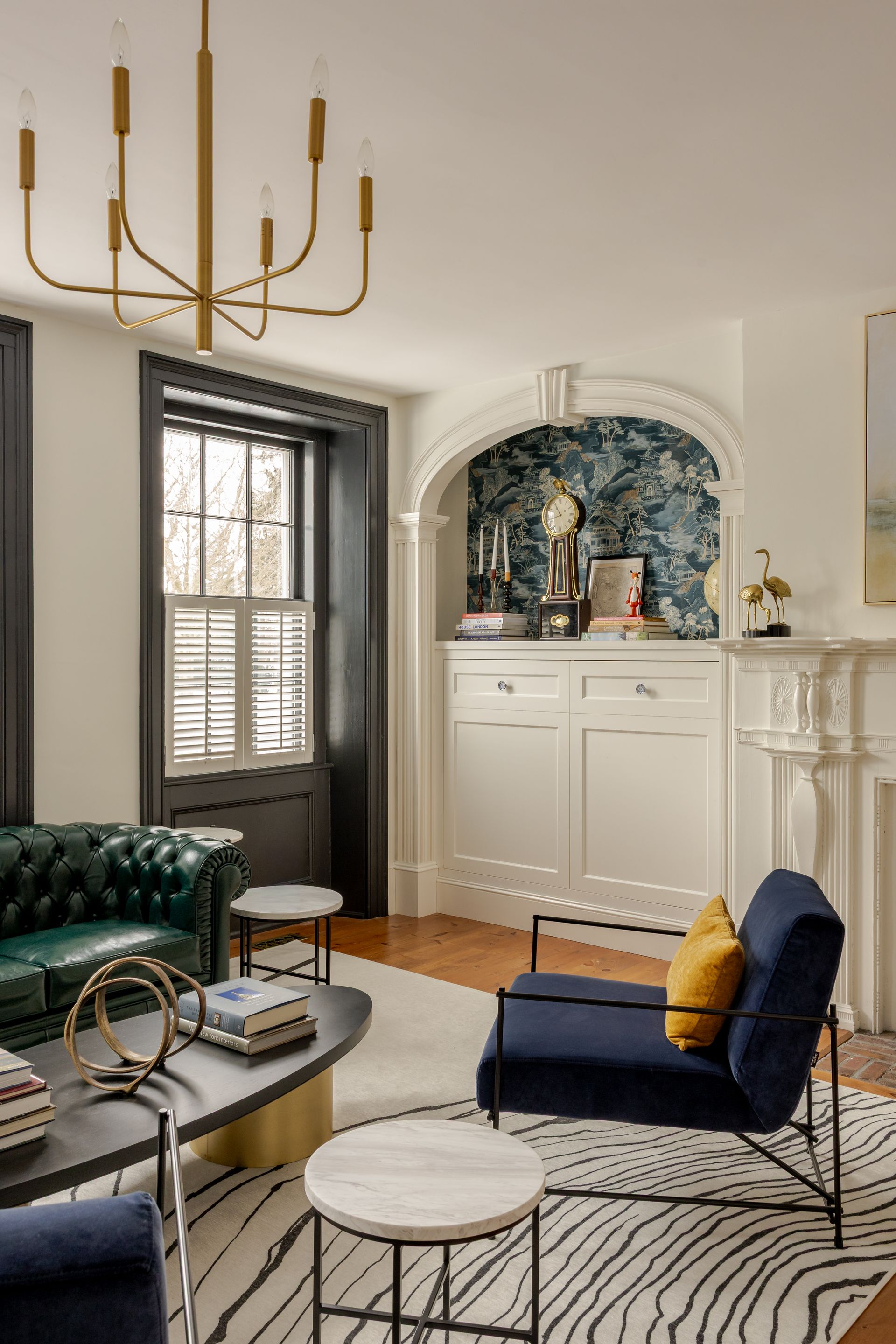 A living room with a green tufted sofa, a navy armchair with a yellow pillow, a patterned rug, and an arched built-in.